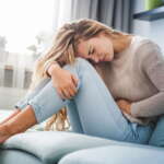Endometrioza - młoda kobieta siedząca na sofie trzymająca się za bolący brzuch.