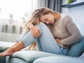 Endometrioza - młoda kobieta siedząca na sofie trzymająca się za bolący brzuch.